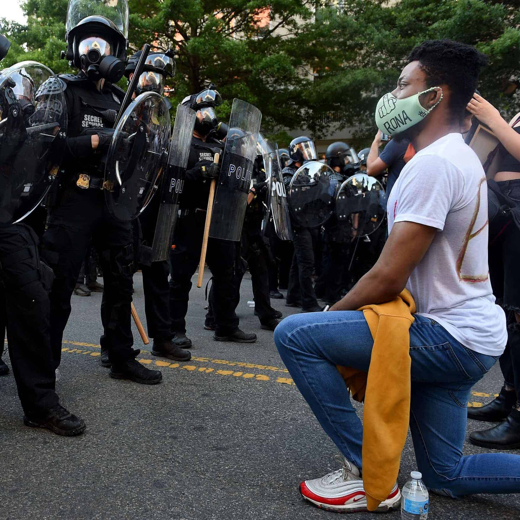 A protester kneels in front of a row of police.