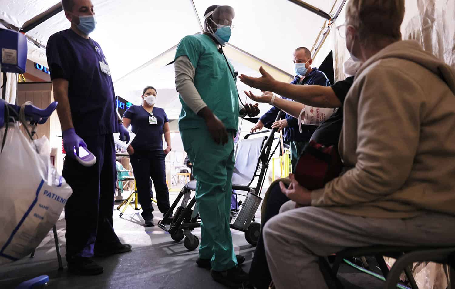 Clinicians evaluate an incoming patient with his arms raised in a triage tent set up in the parking lot at Providence St. Mary Medical Center amid a surge in COVID-19 patients.