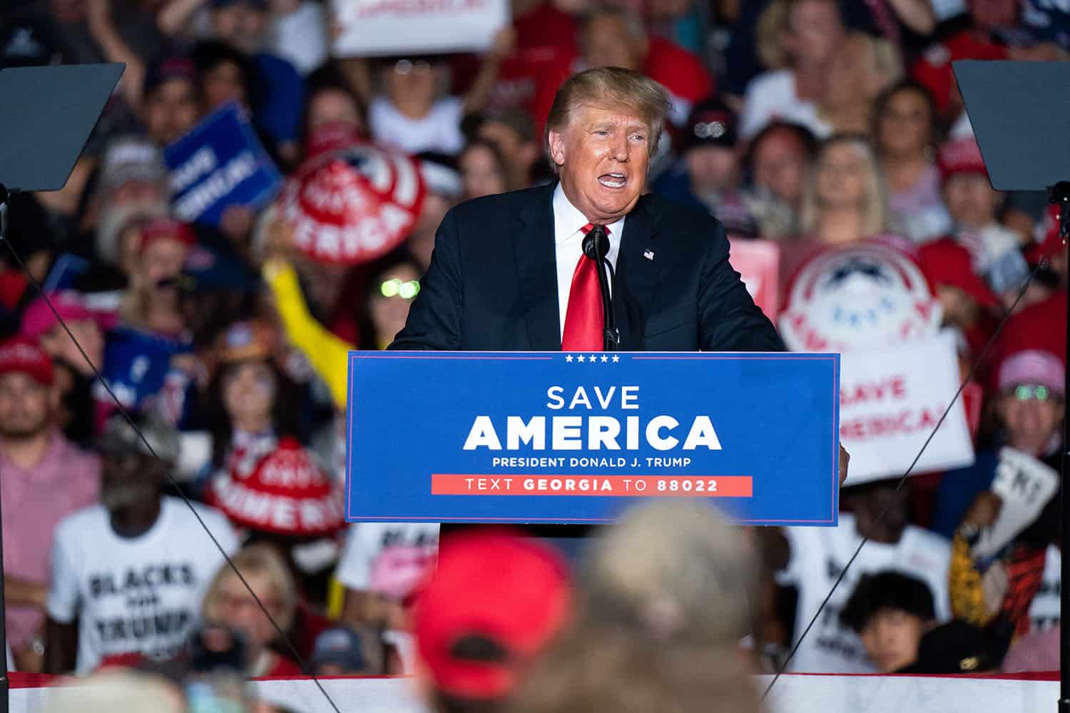 Former President Donald Trump speaks in front of a podium at a rally.