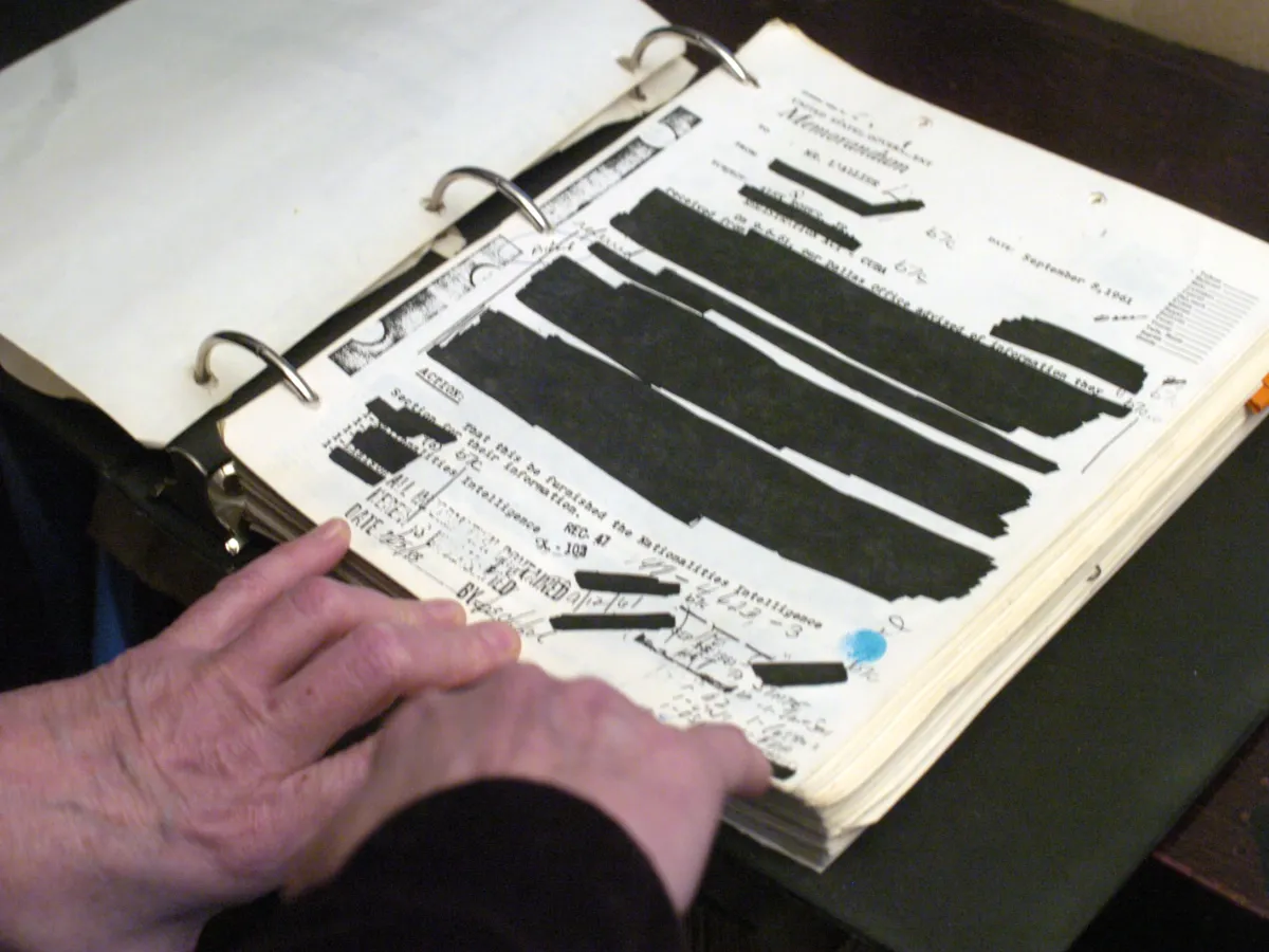 Redacted documents are in a binder.