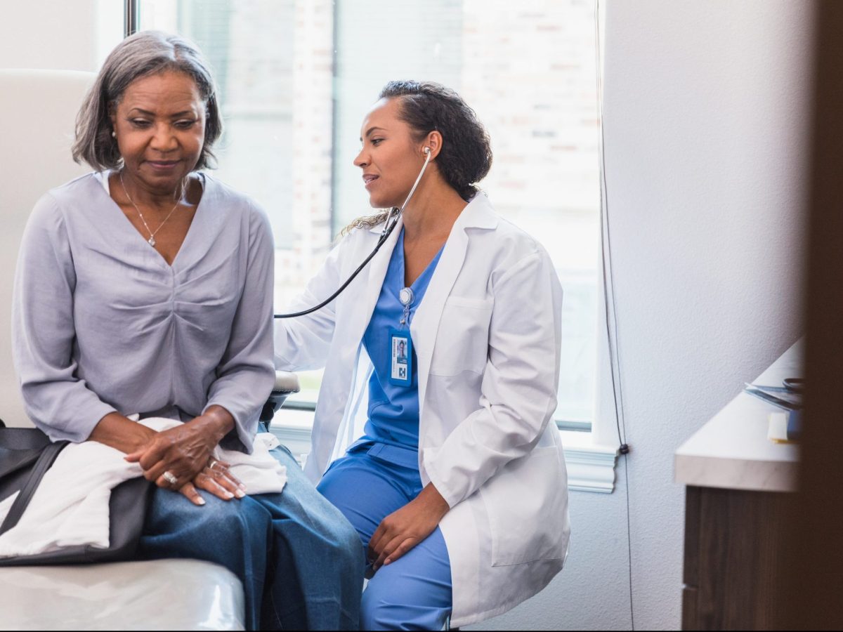 A mid adult female doctor uses a stethoscope to listen to a senior female patient's lungs during a medical exam.