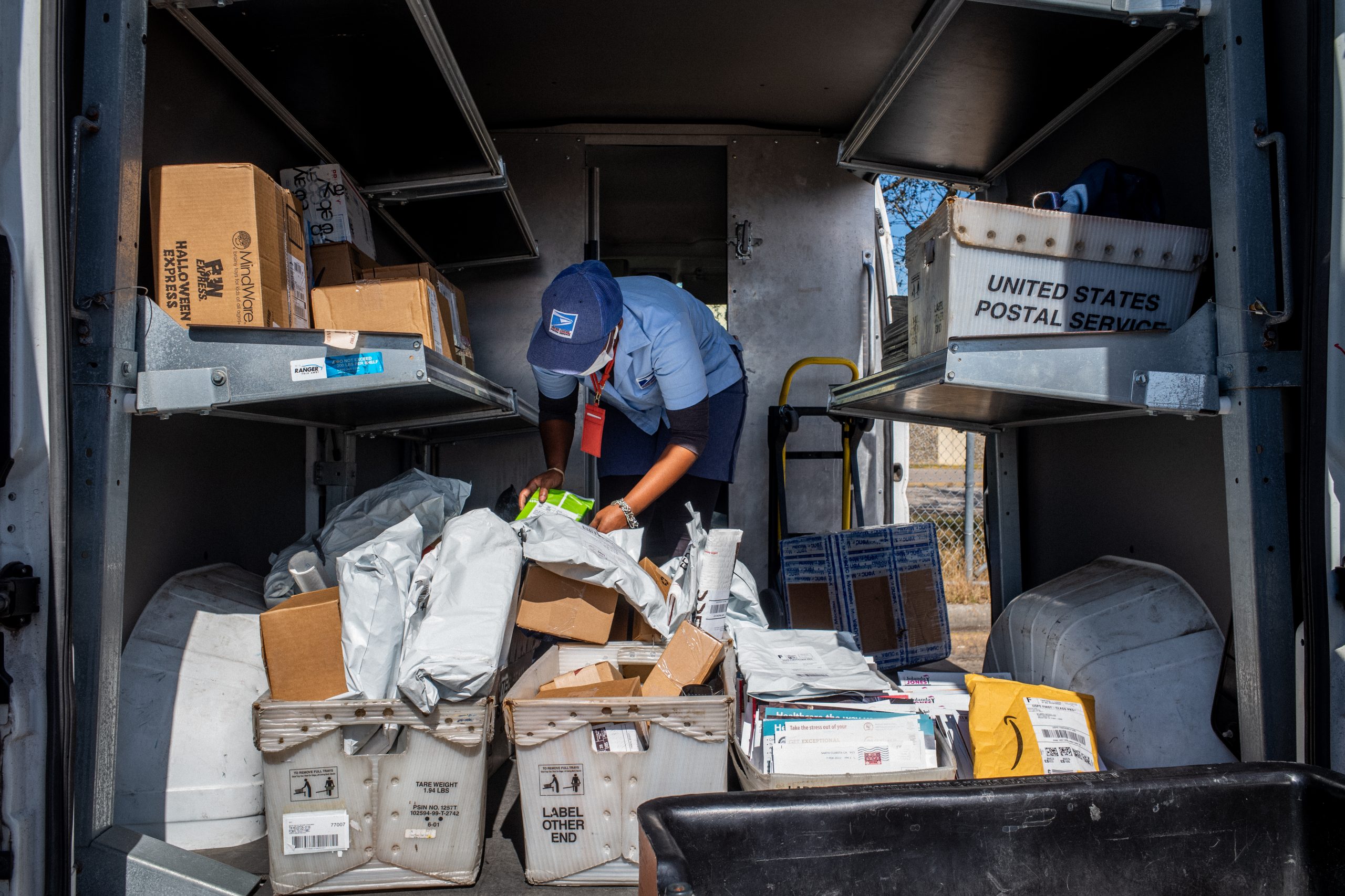 A mail carrier sorts through mail in the back on a postal vehicle.