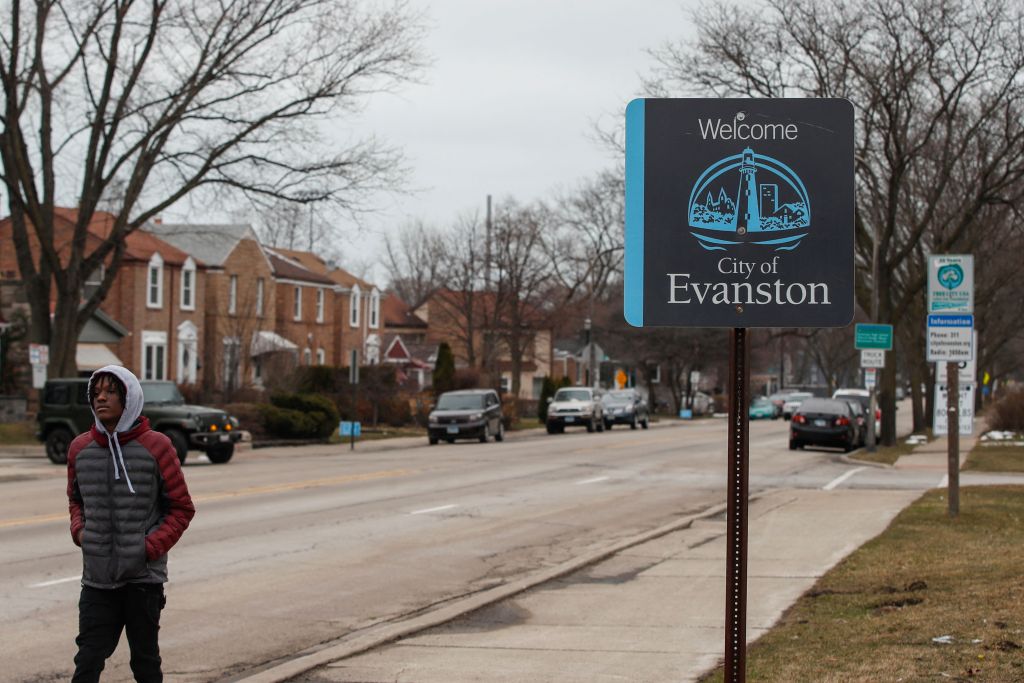 A man walks by a sign that says "Welcome. City of Evanston".