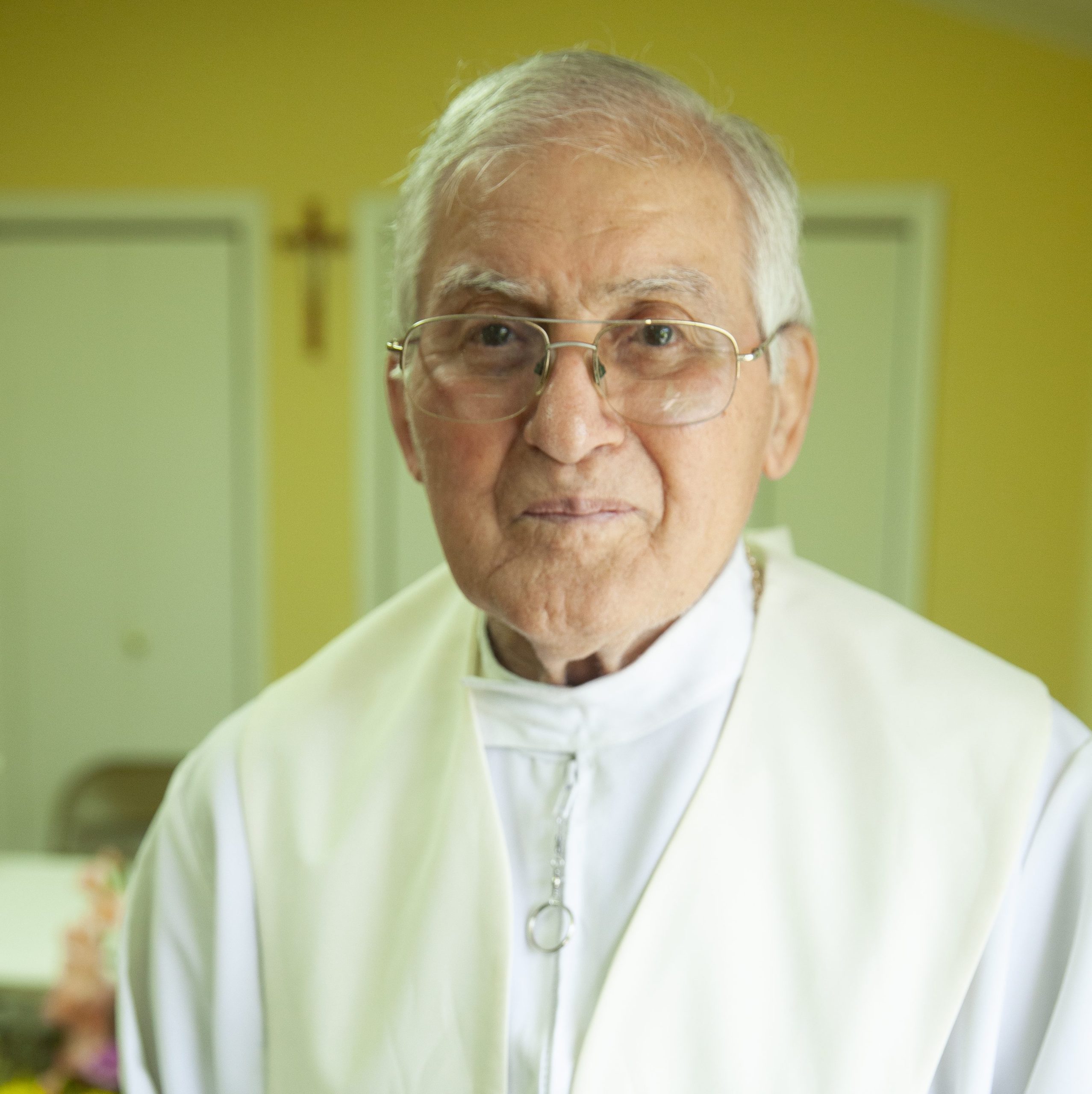 The Rev. Roch Naquin smiles as a cross is seen behind him in the background.