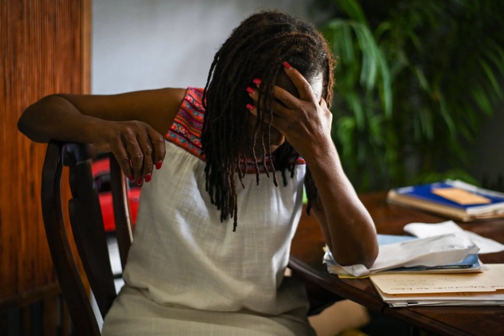 Woman sits at desk with folders and papers on it with her head in her hands.