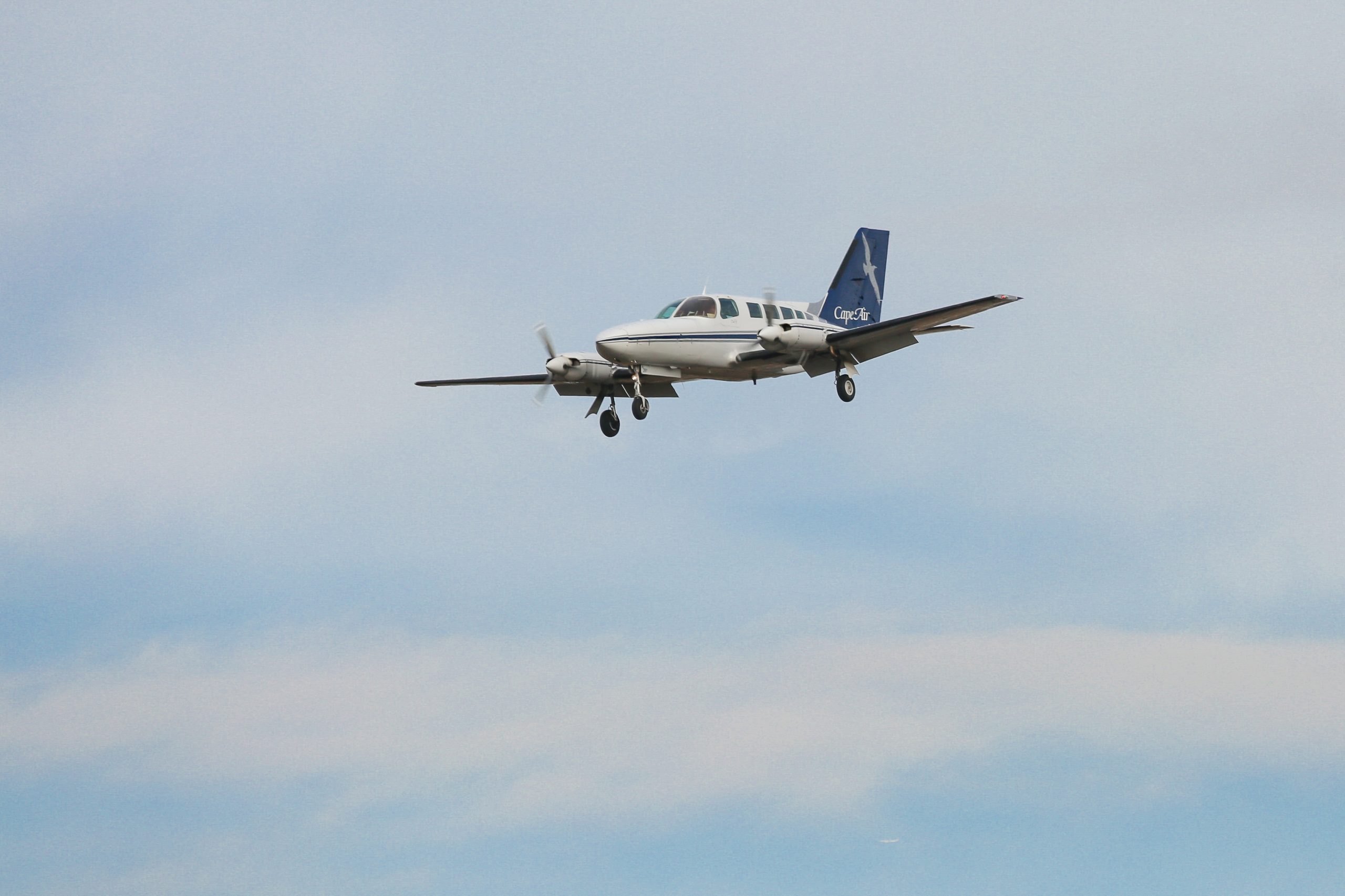 A piston-engine aircraft flies against a cloudy sky