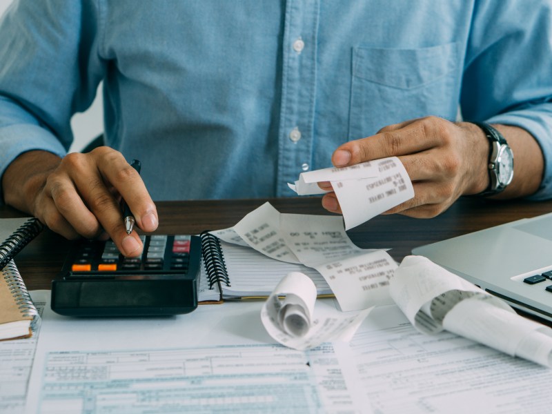 A person sits at a table looking over receipts will using a calculator.