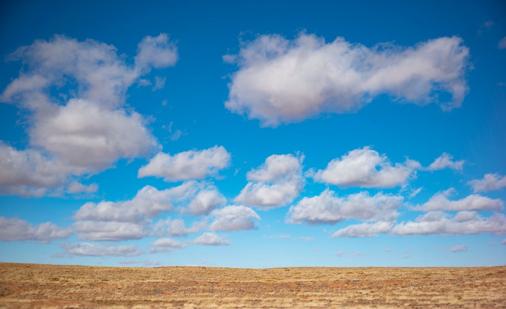A blue sky with fluffy clouds, against the light brown of the earth.