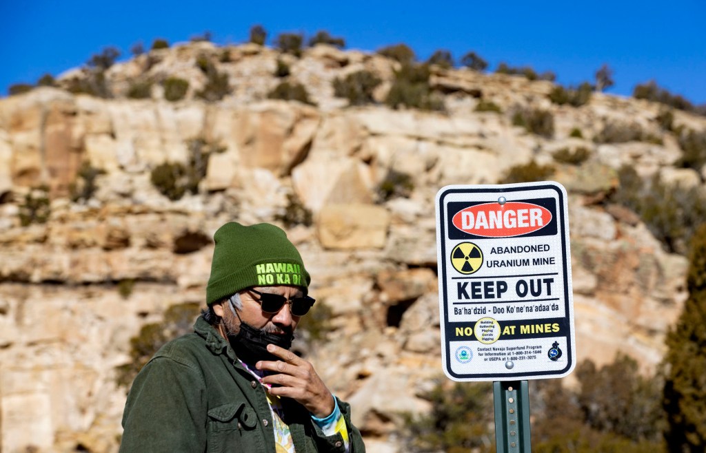 Earl Tulley, wearing a green hat that says "Hawaii No Ka Oi," sunglasses and a face mask to protect from COVID-19, pauses near a sign that says: "DANGER: Abandoned uranium mine. KEEP OUT."