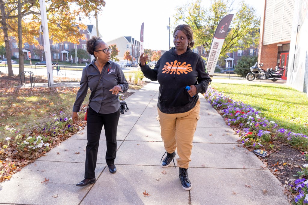 L'Tanya Holley looks at Towanda Chew as they walk on a sidewalk, Chew gesturing as she talks.