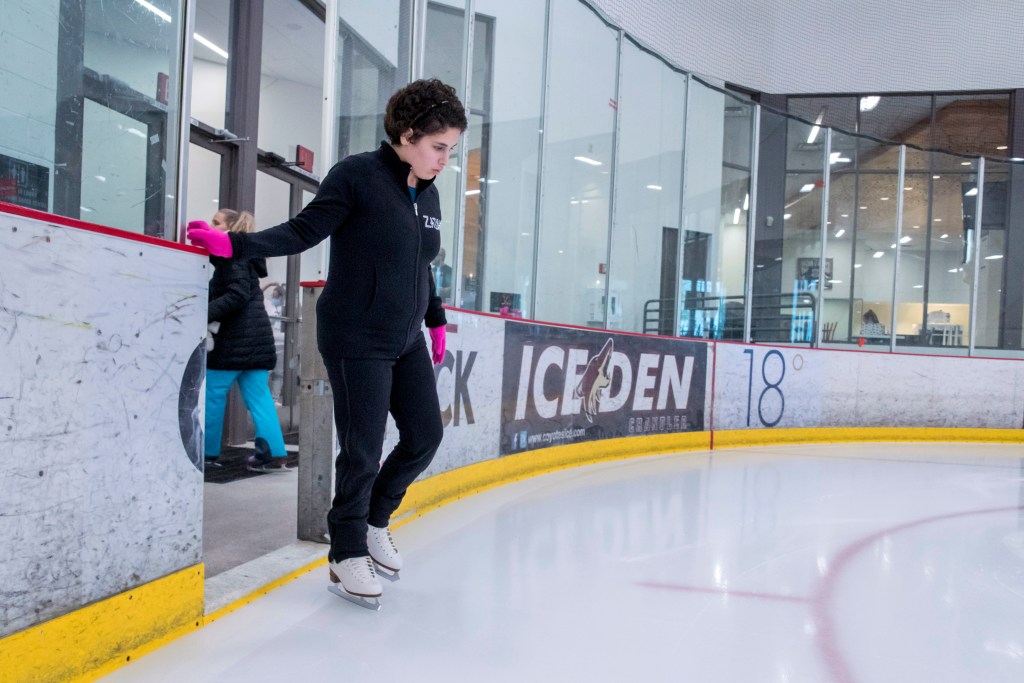 Zainab Edwards stands ready to take the ice. She is wearing a black sweatshirt, black pants and pink gloves.
