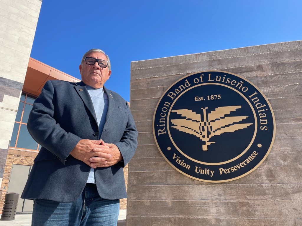 Bo Mazzetti stands outside the tribe’s government center, beside a wall with a tribe emblem.