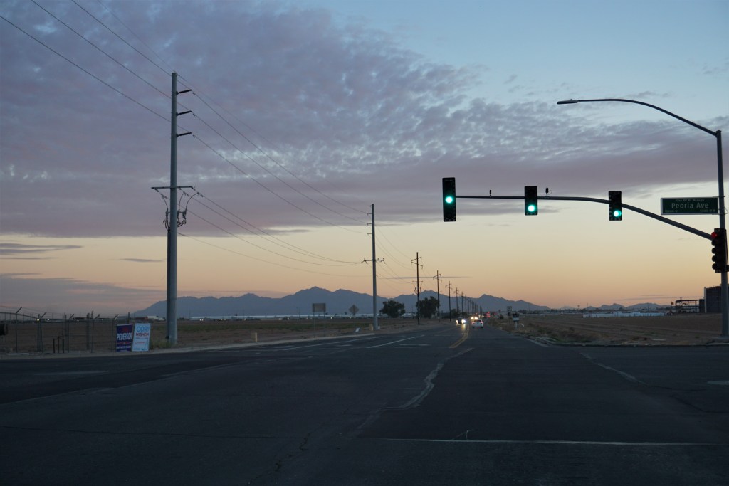 A view from the intersection of a street. The traffic lights are lit green as cars approach the intersection. 