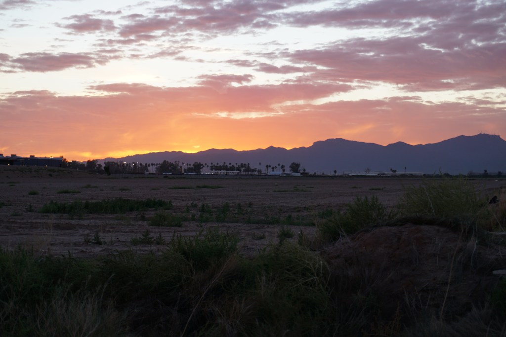 Scrub and mountains are visible in this photo of the sun behind the range, sky rosy