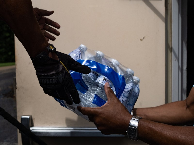 A package of plastic water bottles exchanges hands between two people.