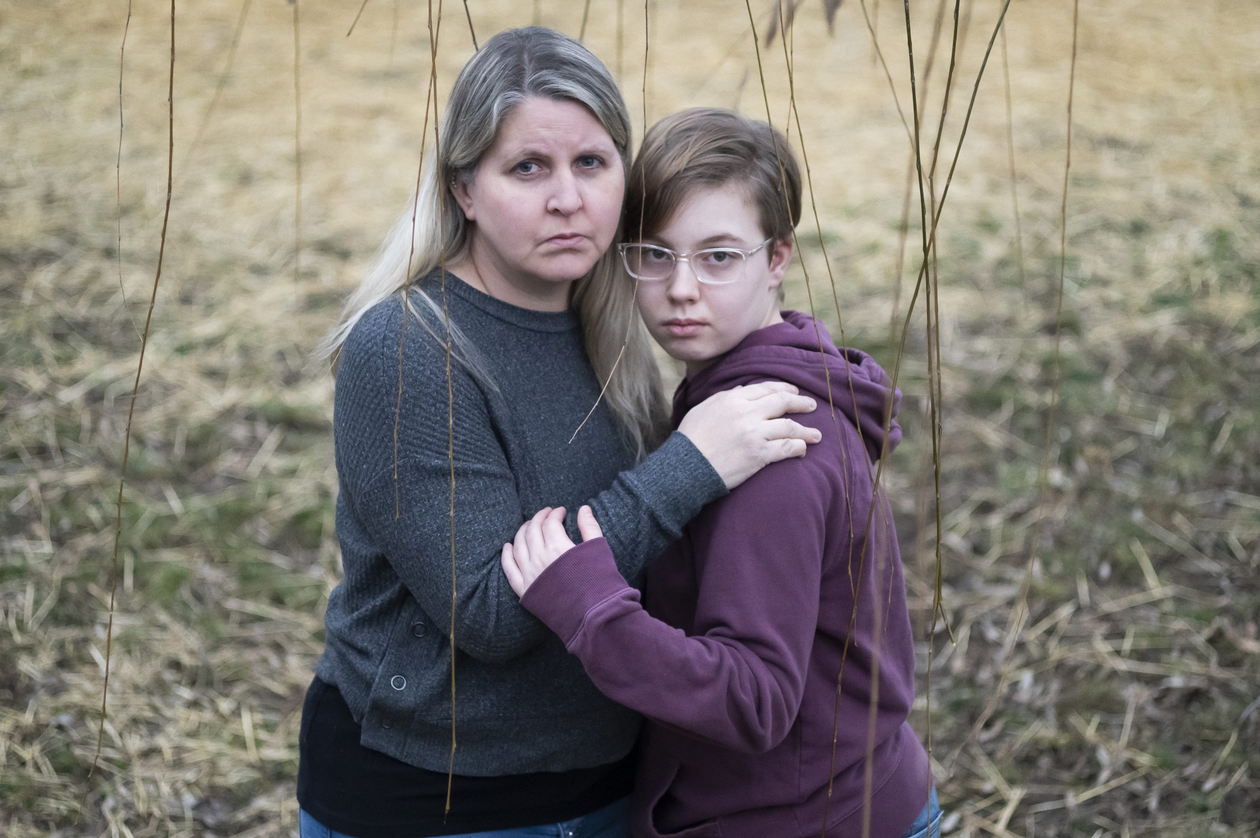 Lisa Norris stands hugging her daughter Hannah. Lisa has long blond hair and is wearing a blue sweater. Hanna has short brown hair and wears glasses and a purple hoodie.