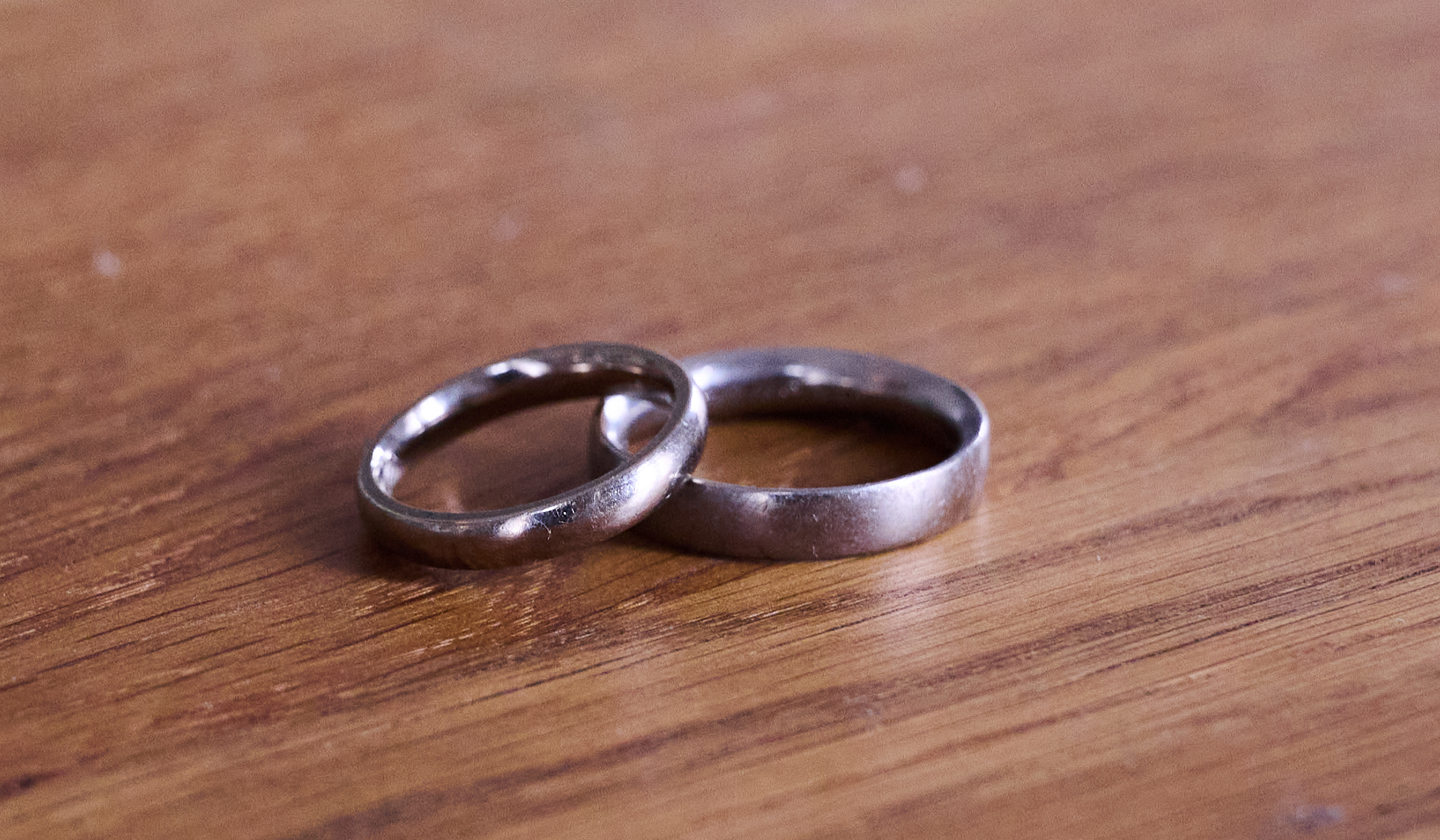 Two silver wedding rings lie next to each other on a wooden table.