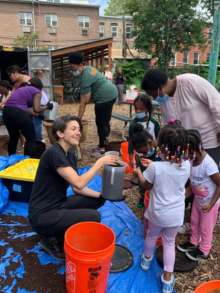 Sara Perl Egendorf is bent down as she shows a group of young children and one adult soil that has been collected in a rubber container.