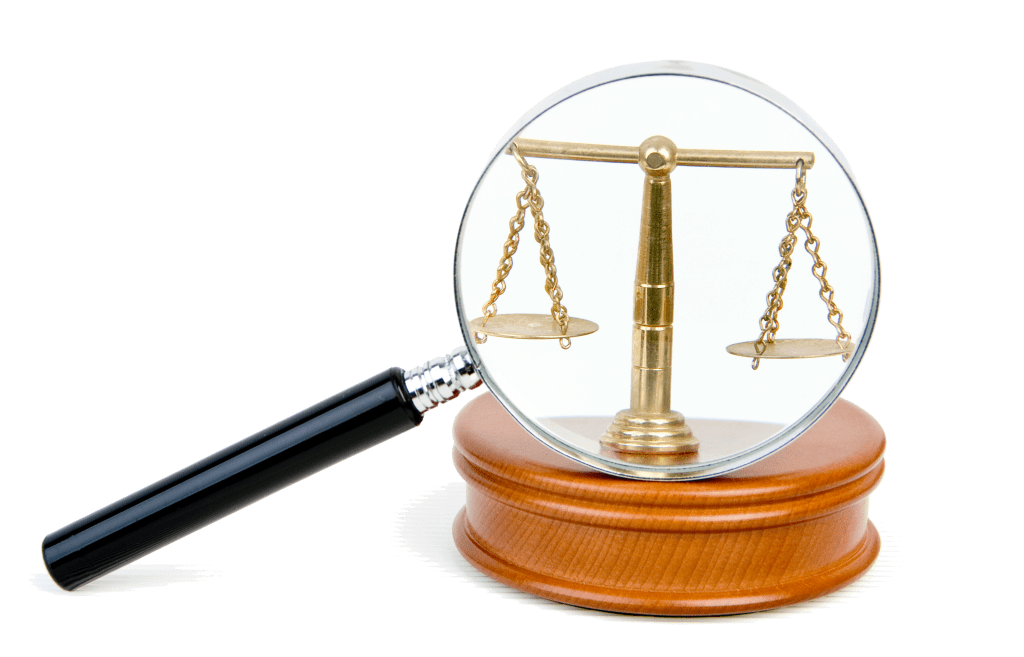 A magnifying glass sits atop a gavel. The scales of justices is magnified in the magnifying glass. 