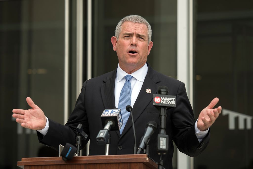 Philip Gunn is standing behind a lectern with television station microphones. He is talking and has his hands spread.
