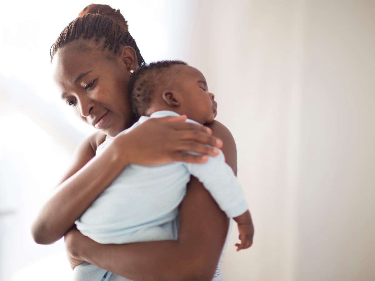 Black mother holds her sleeping baby in front of a white background.