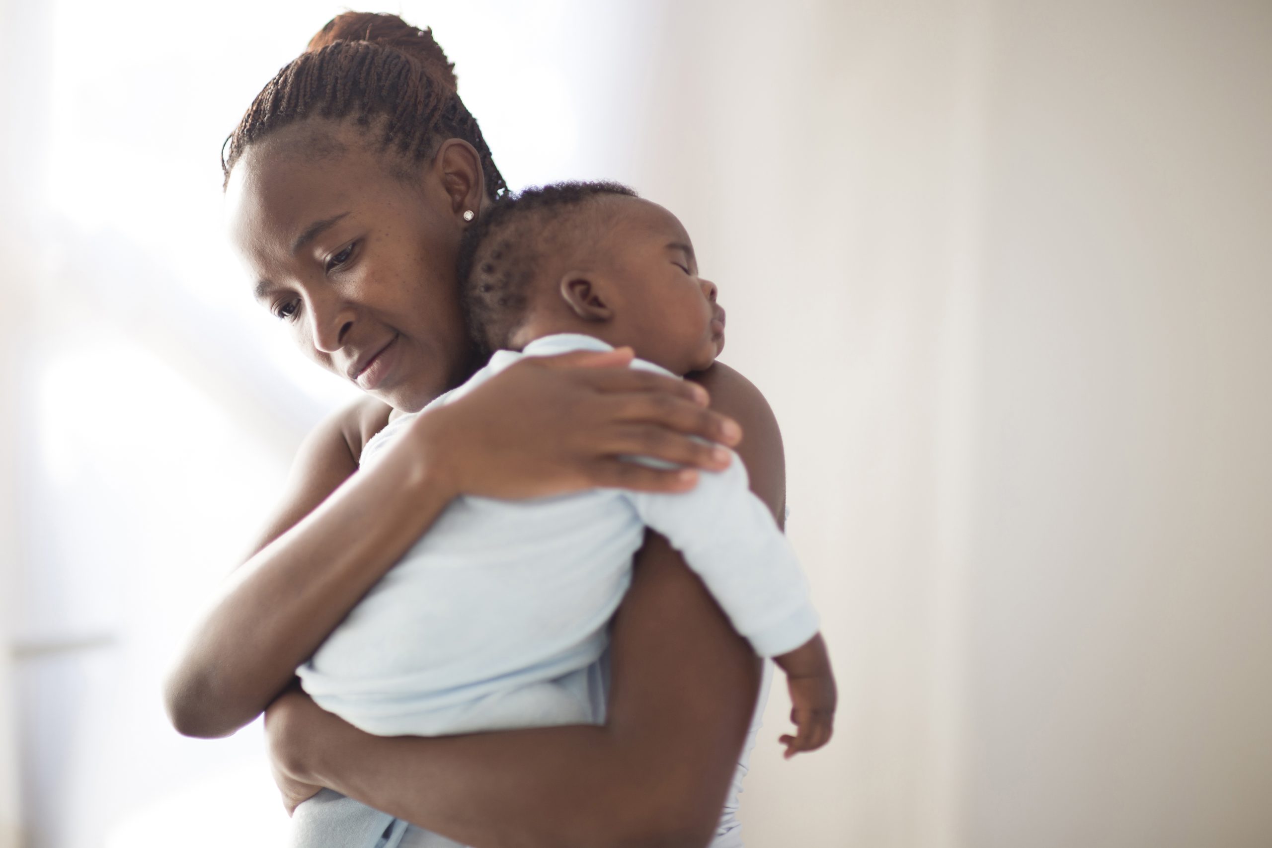 Black mother holds her sleeping baby in front of a white background.