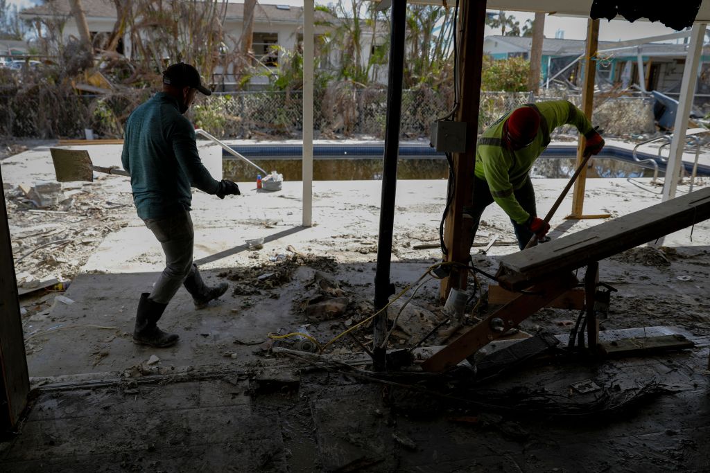 One worker uses a shovel to clean up debris, while another walks by with a shovel in his hand at a cleanup site. 