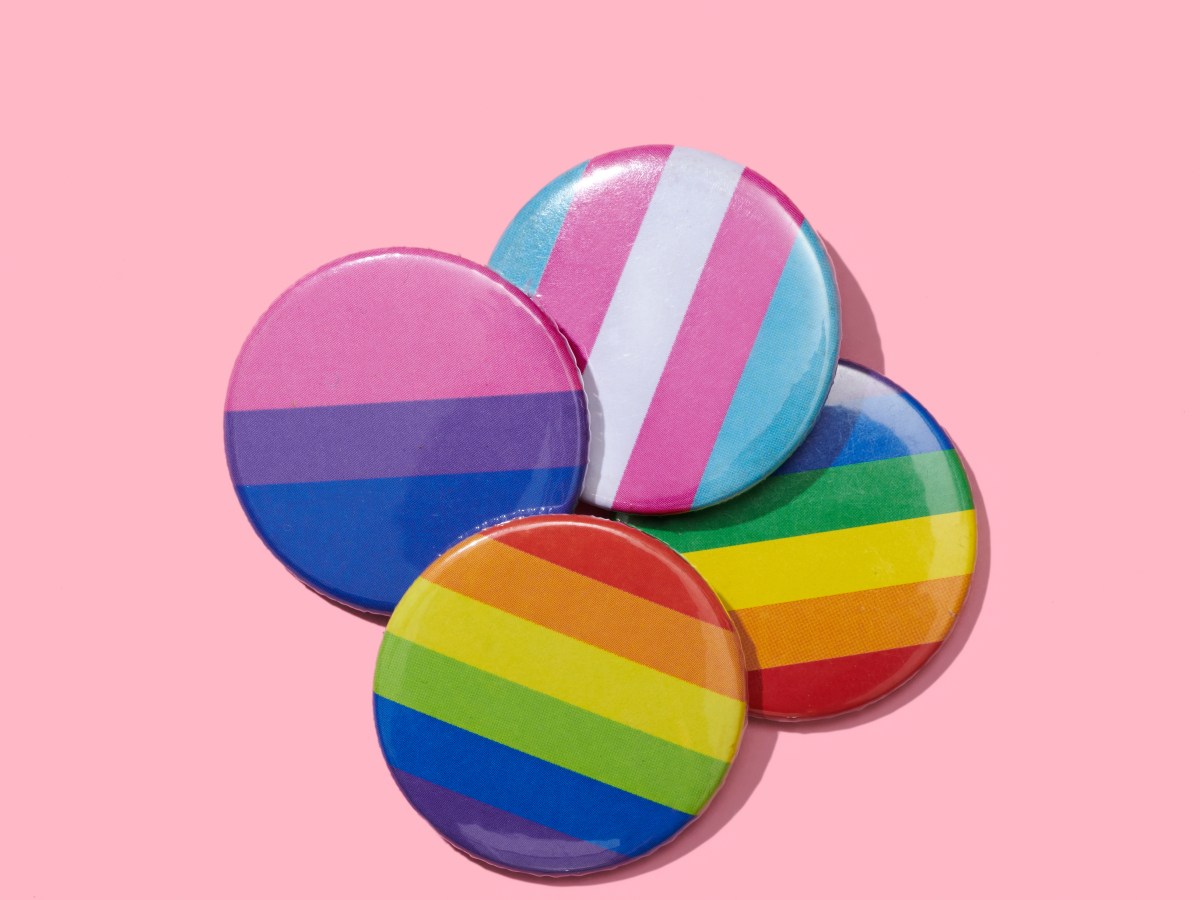high angle view of some pin buttons patterned with different LGBTIQ flags, such as the gay pride flag, the transgender pride flag or the bisexual pride flag, on a pink background