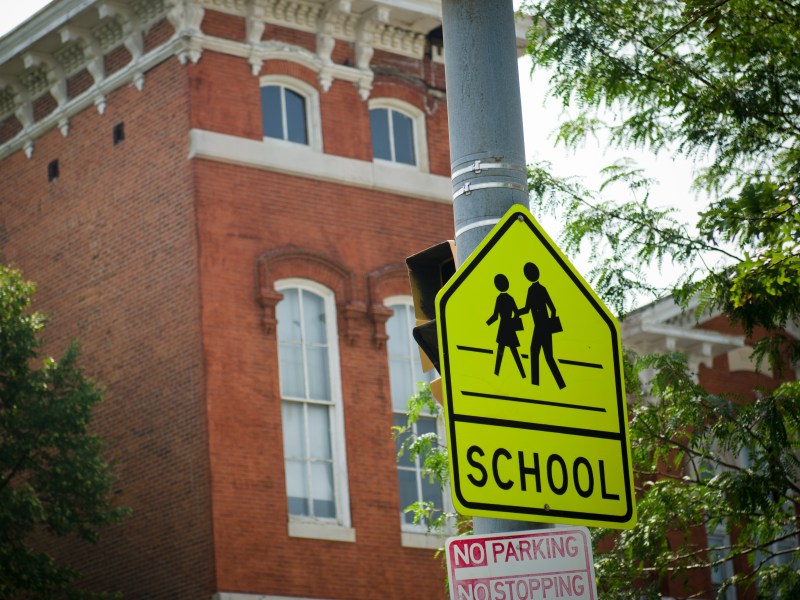 A neon yellow 'children crossing road sign' on a street pole in front of a red brick building.