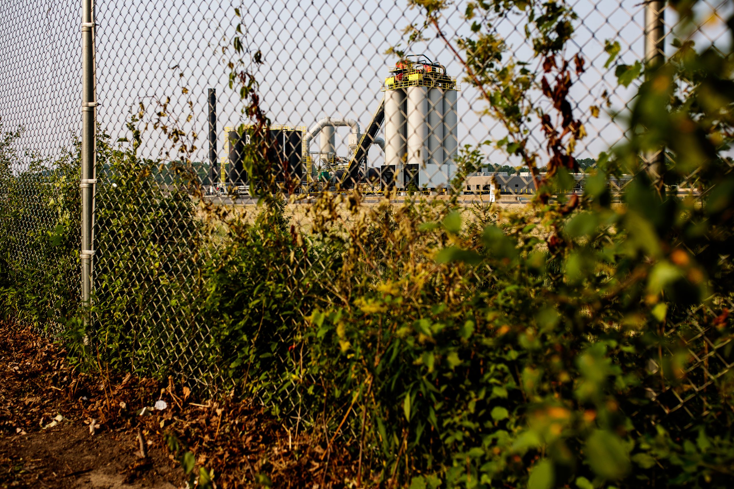 Several black and white silos (one labeled AJAX) line an industrial park that is behind a fence.
