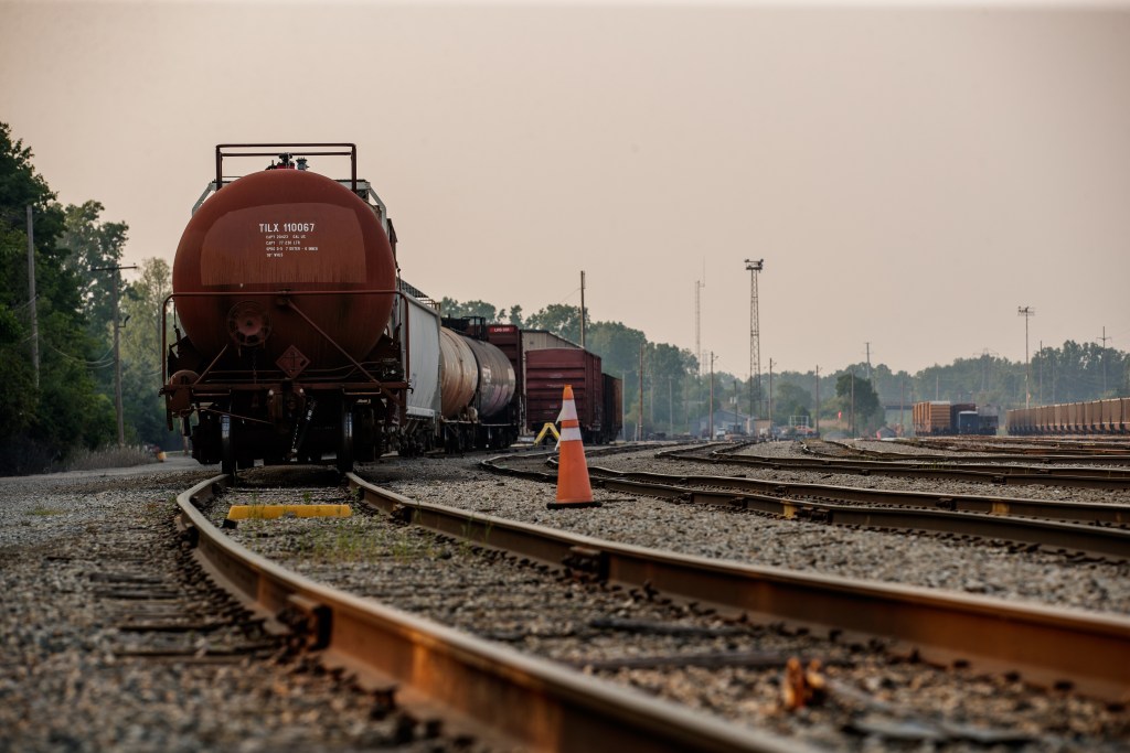 In the foreground is a hauling train that sits on the tracks. In the background are other idle trains on tracks.