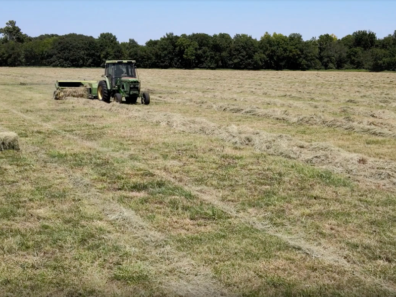 A green tractor picks up hay on a sprawling farm.