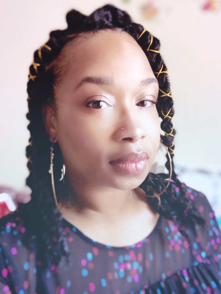 Amanda looks straight to the viewer. She is wearing a polka dot top with hoop earrings.