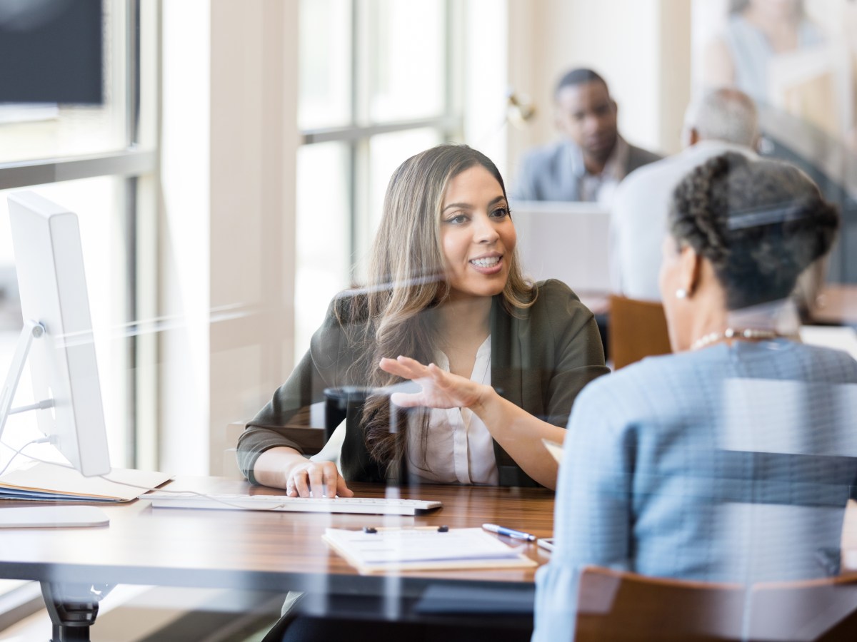 Two Black women discuss banking in this photo, taken in a corporate setting with light coming in through windows