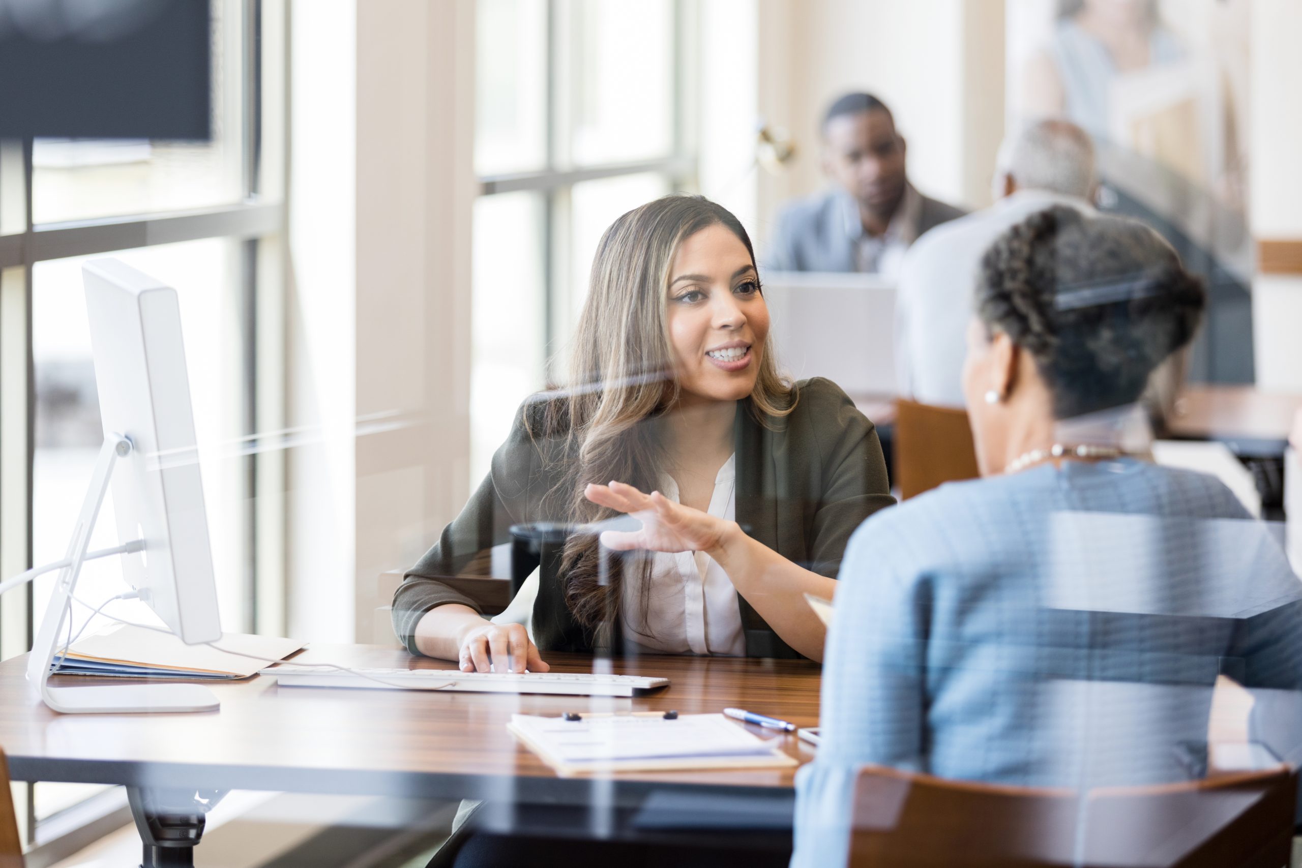 Two Black women discuss banking in this photo, taken in a corporate setting with light coming in through windows