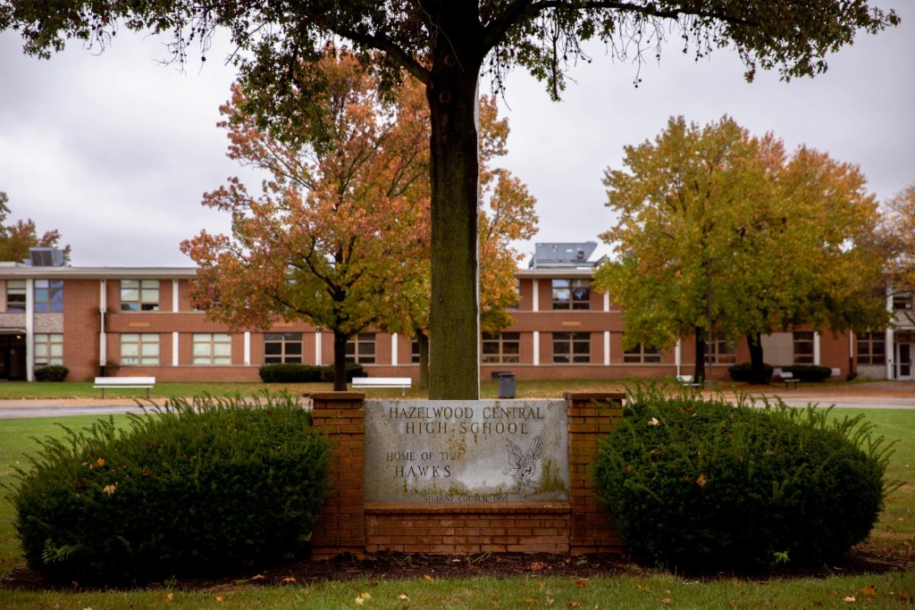 Photo shows a long brick building behind the school sign ("Hazelwood Central High School, home of the Hawks")