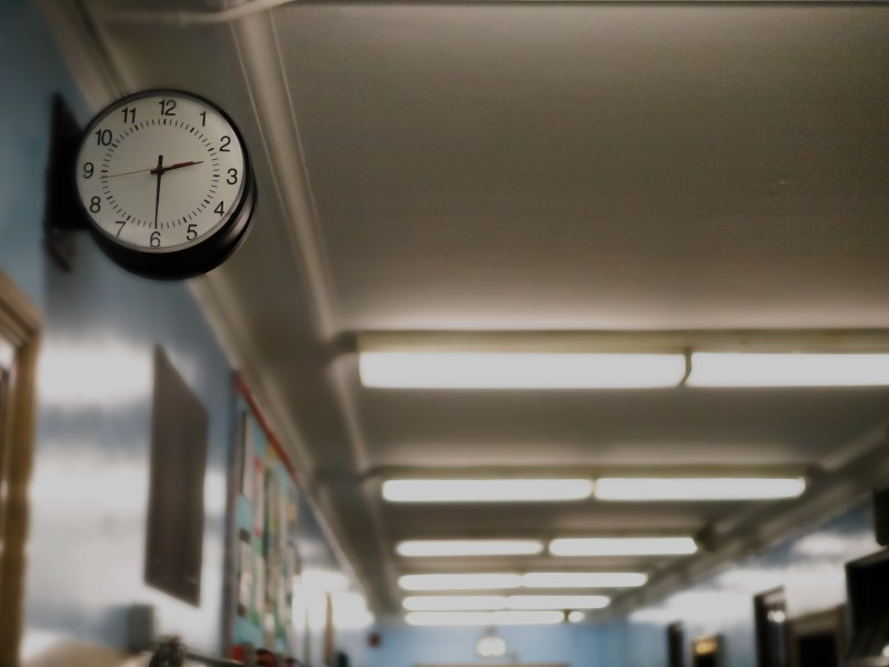 A clock is visible in the foreground of a photo in a school hallway