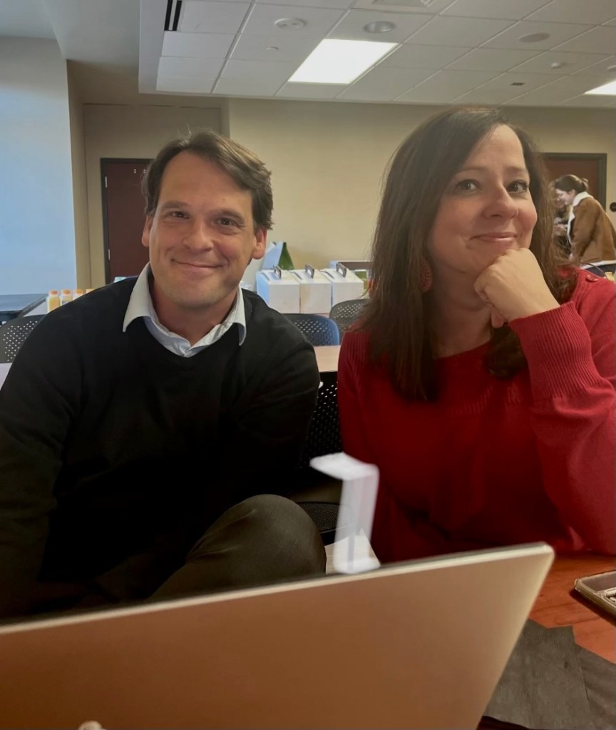 Lisa Yanick Litwiller and Matt DeRienzo are sitting beside each other an indoor setting behind a laptop.