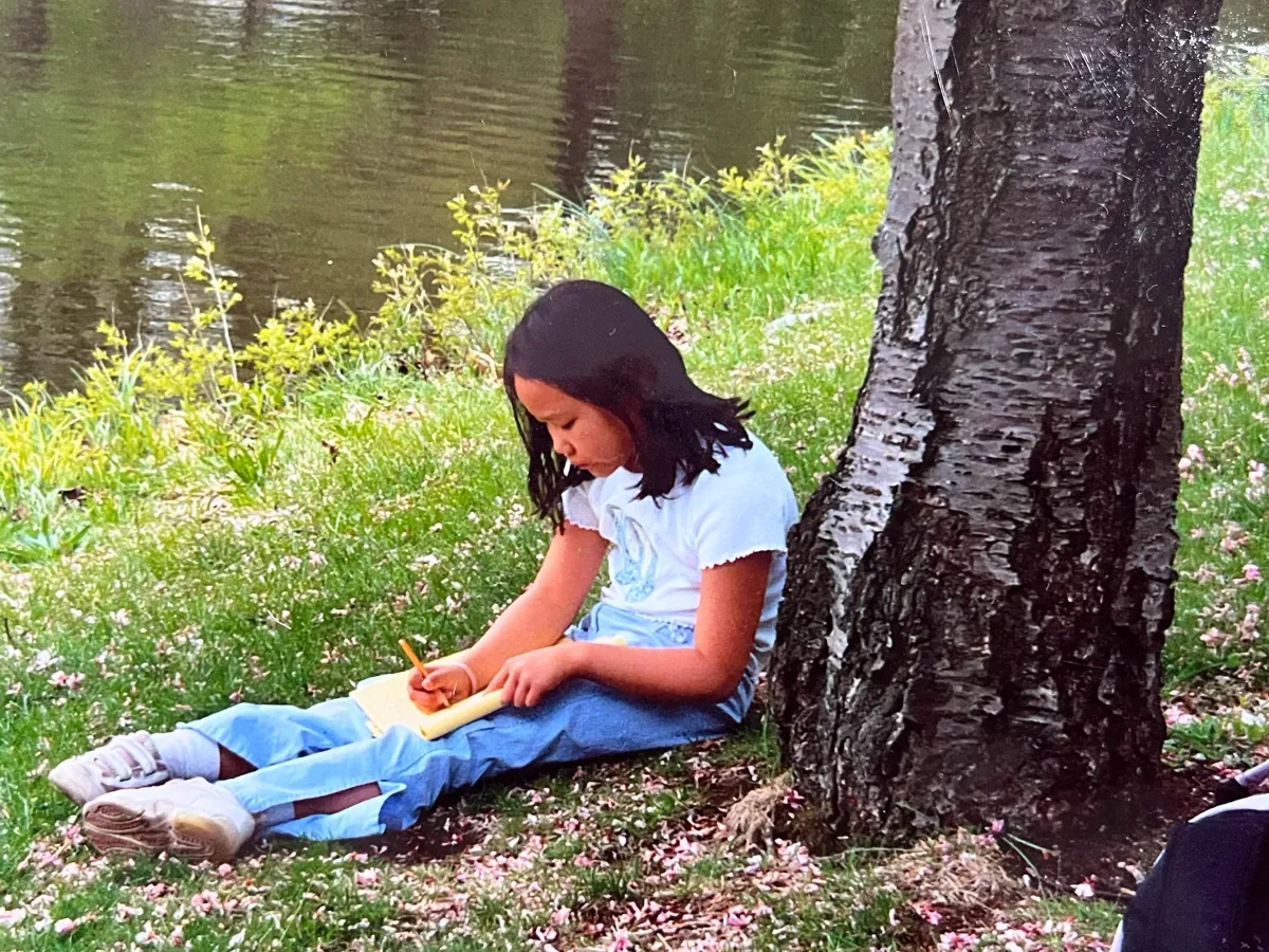 Lian is looking down at the notepad in her lap, holding a pencil