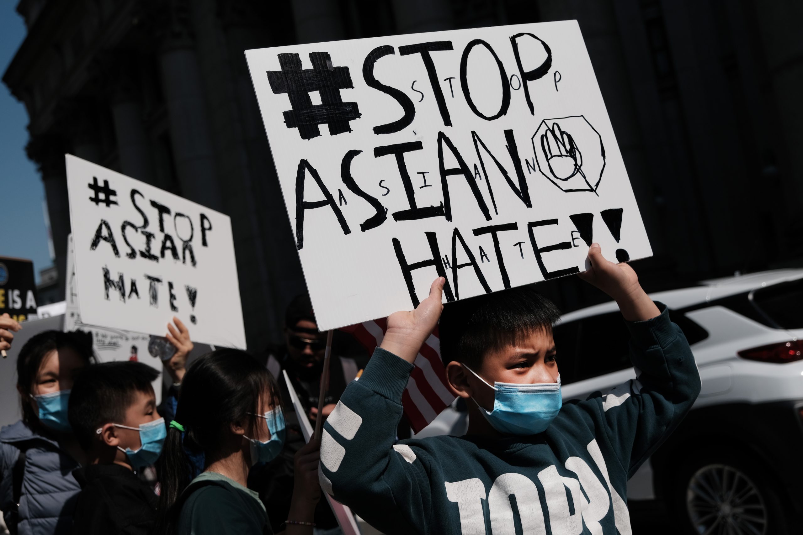 Several children, two holding "Stop Asian Hate" signs, are visible in the close-up shot of the protest.