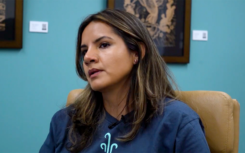 A young woman sits in a brown leather chair. She is wearing a blue shirt and has medium length hair. She looks off to the side.
