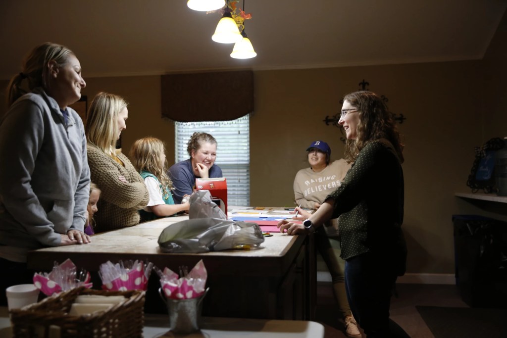 a group of women and girlds stand around a table laughing